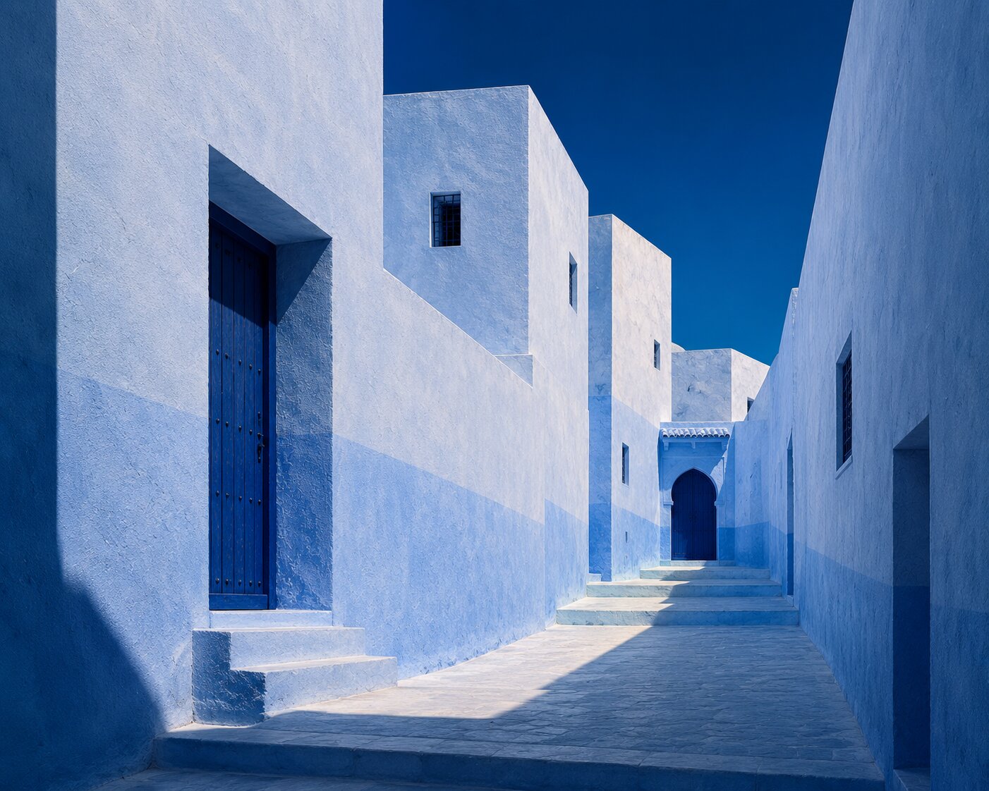 Narrow Chefchaouen passage with white and blue façades and a blue door in the distance.