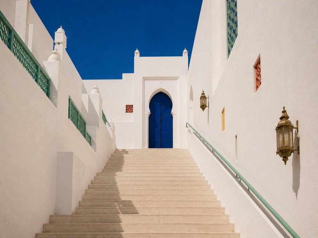 Escalier blanc montant vers une porte bleu cobalt, rampes vert d'eau et lanternes dorées sur les murs blancs
