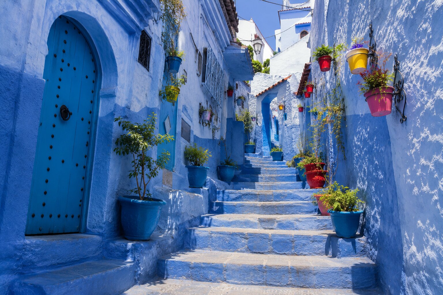 Blue Chefchaouen stairway lined with colourful pots, plants and a turquoise door.