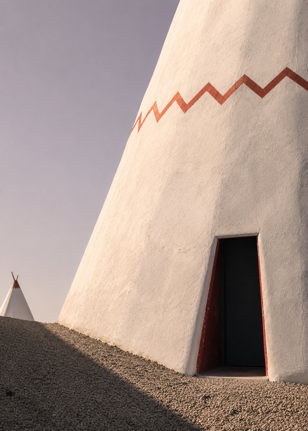 Ivory conical wall of the Wigwam Motel, red zigzag motif and dark doorway in Holbrook.
