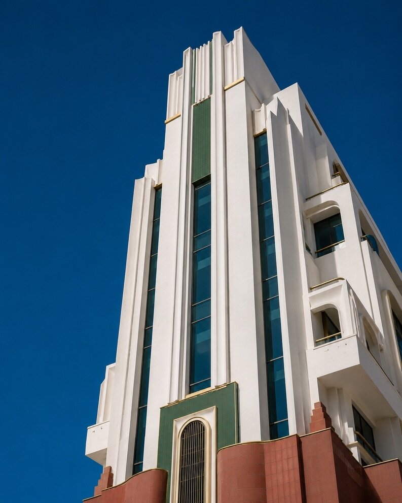 Tour moderniste de Casablanca en contre-plongée, lignes verticales blanches, bandes de zellige vert et filets de laiton contre un ciel bleu profond