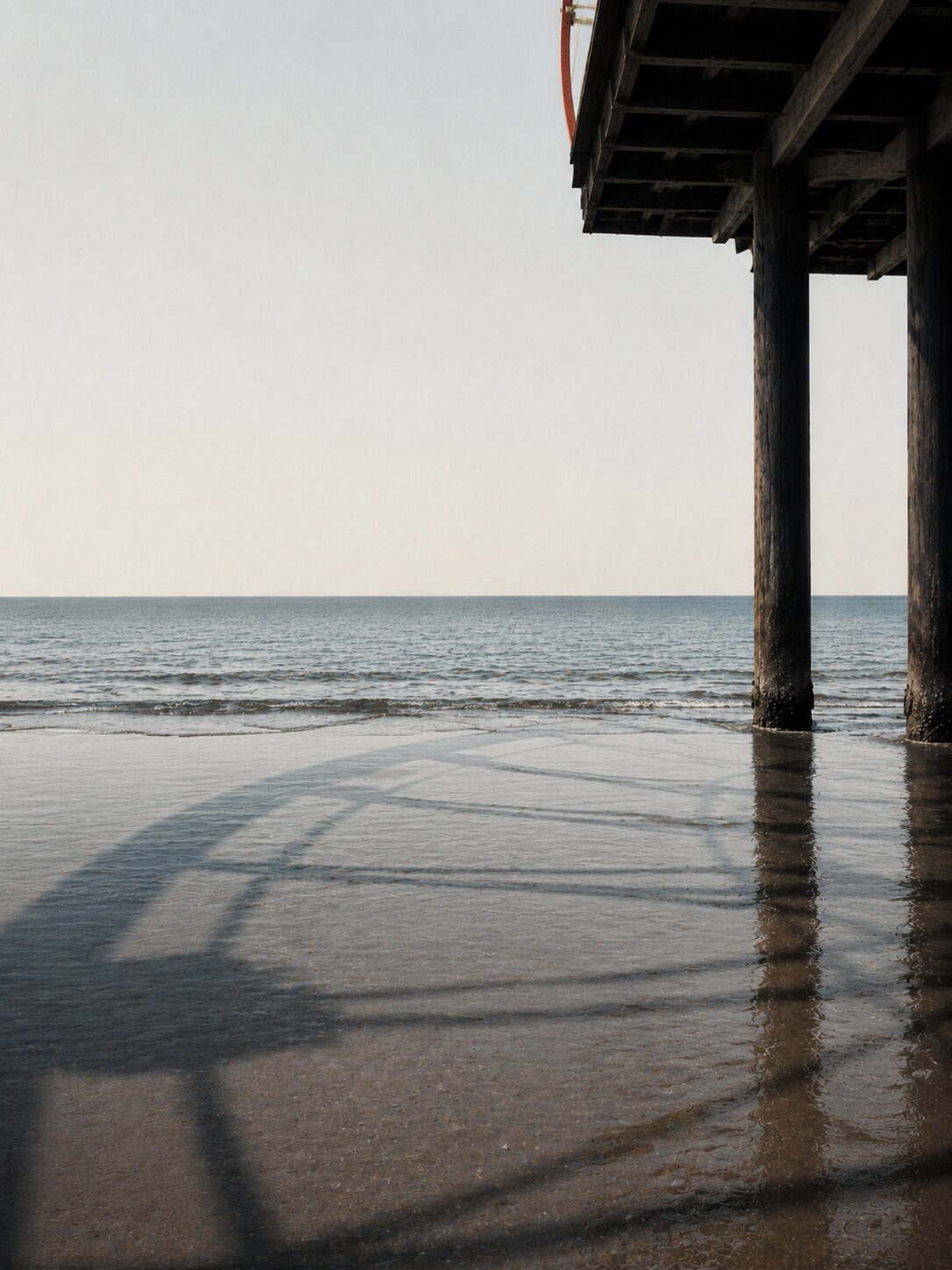 Santa Monica pier columns, long shadow across wet sand and the Pacific horizon.