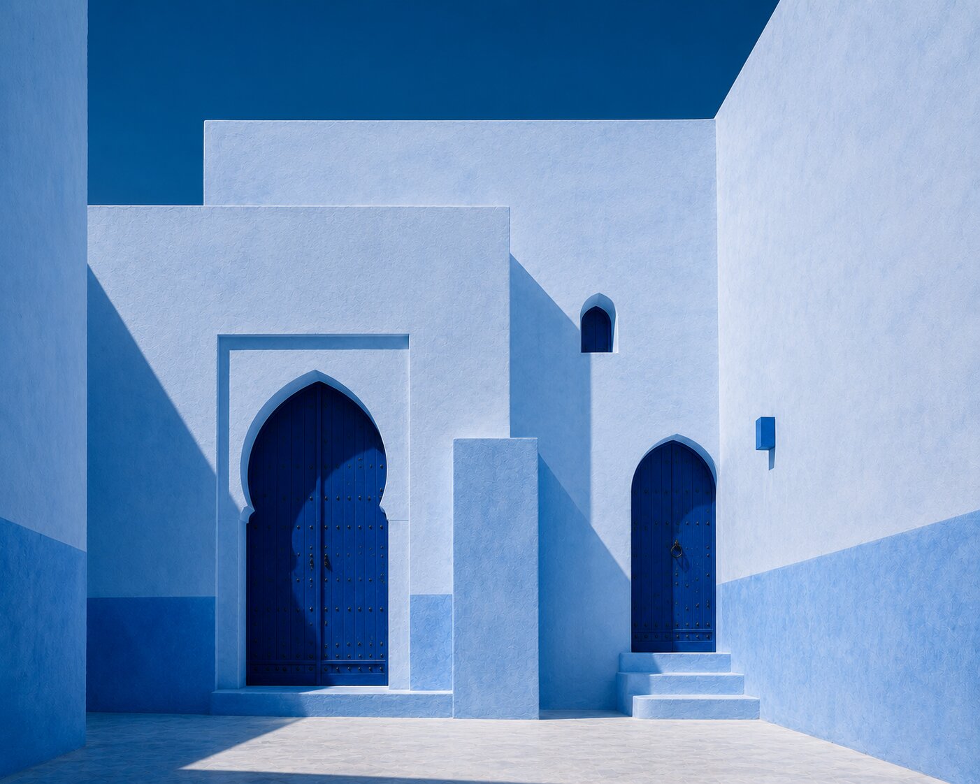 Two deep blue arched doors in a minimalist white and blue Chefchaouen courtyard.